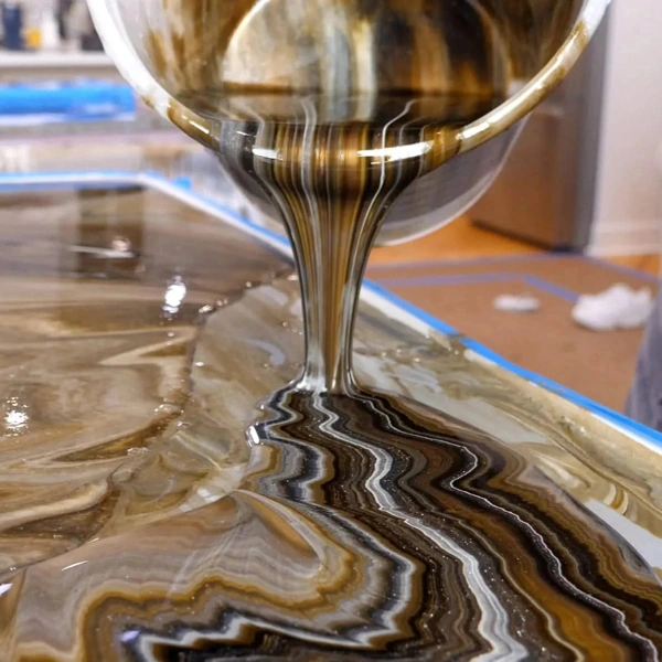 Pouring metallic epoxy floor coating in gold and black.